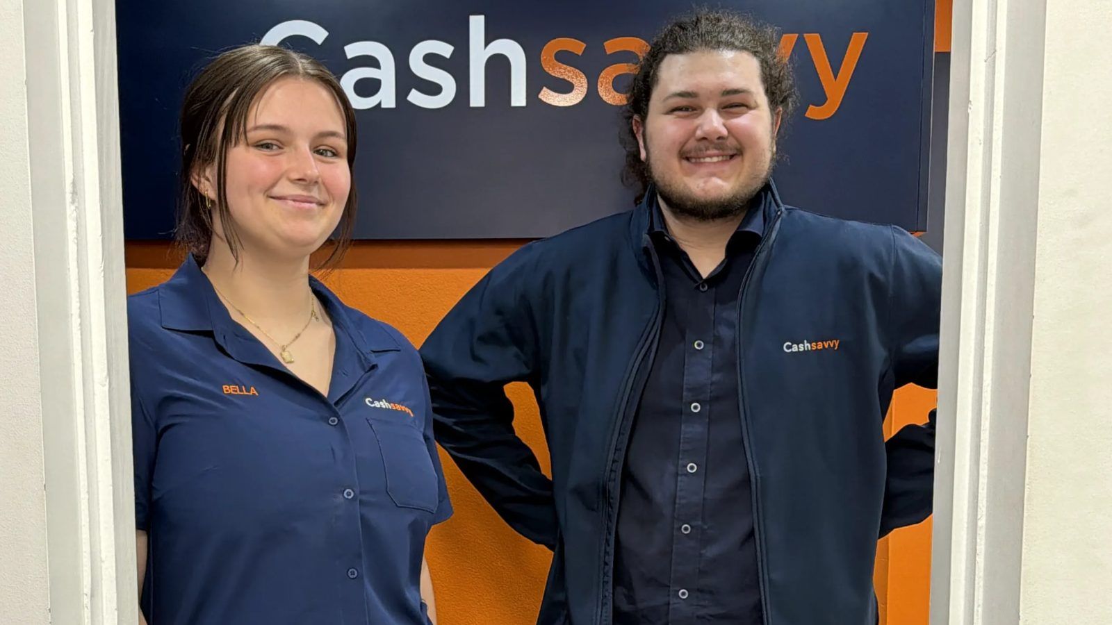 Two Cash Savvy staff in branded uniform shirts and jacket at the store entrance