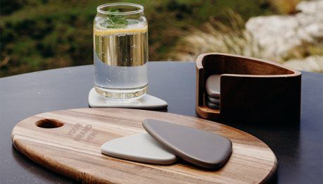Premium corporate gifts on a timber board including a leather coaster set and glassware