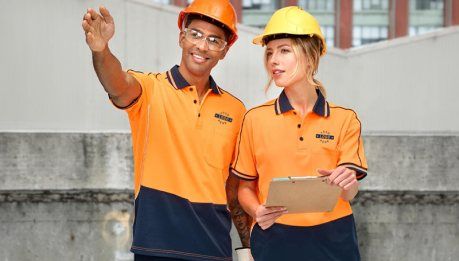 Two construction workers in hi-vis orange polo shirts and hard hats on site
