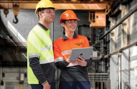 Two site workers in hi-vis jackets reviewing plans on a tablet